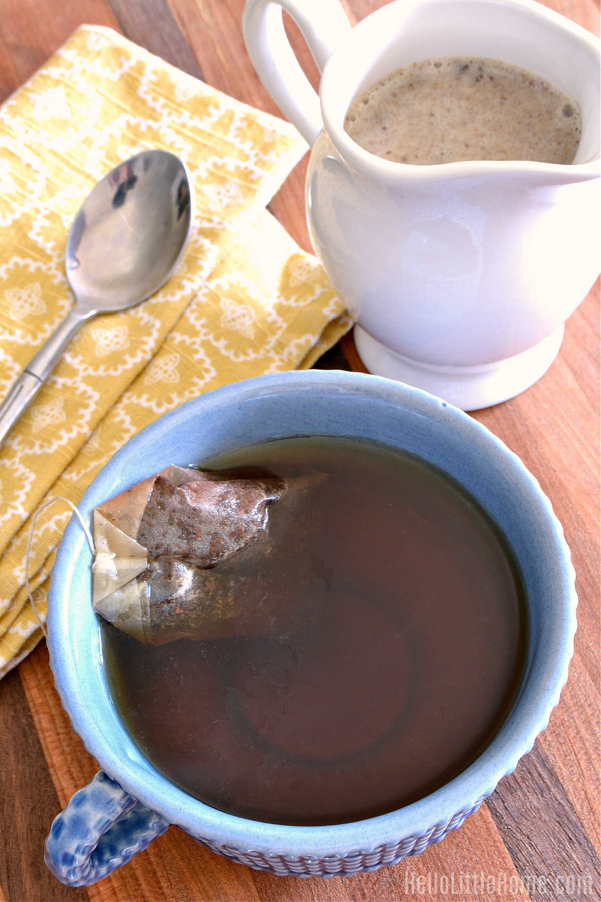 A mug of tea, chai syrup, napkin, and spoon on a wood table.