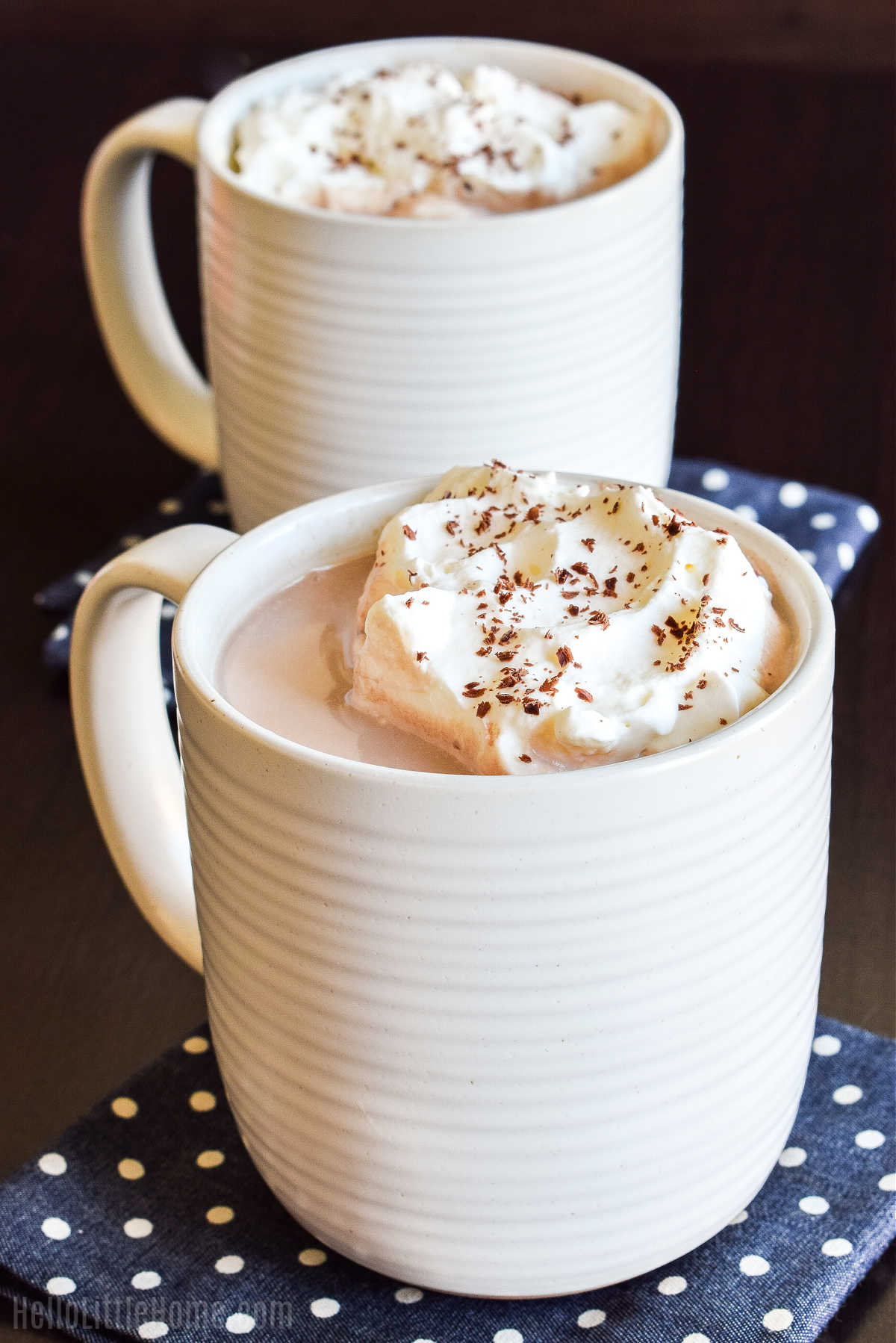 Mugs of the finished drink topped with whipped cream and served on a dark wood table.