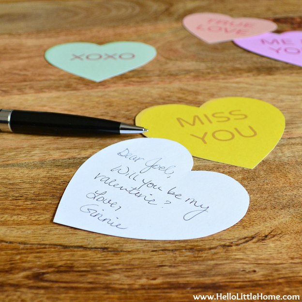A pen next to the cut out hearts on a wood table.