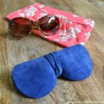 The finished DIY Sunglasses Case on a wood table next to a pair of glasses and a clutch.