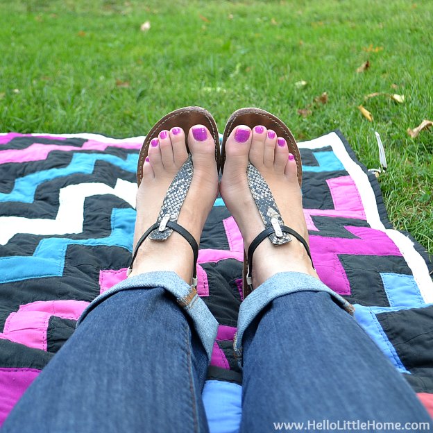 A womans legs on a colorful quilt in the grass.
