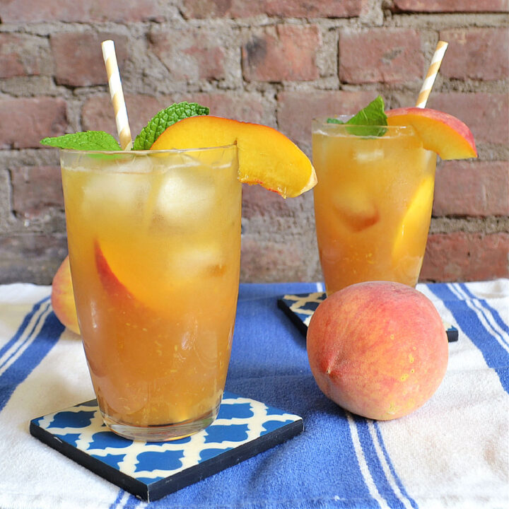 Two glasses of Peach Green Tea served on a striped tablecloth next to a fresh peach.
