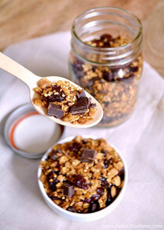 A wood spoon holding a spoonful of granola over a small bowl.