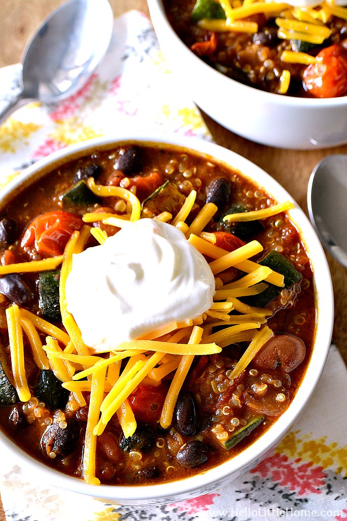 Two bowls of Roasted Vegetable Quinoa Chili with napkins and spoons on a wood table.