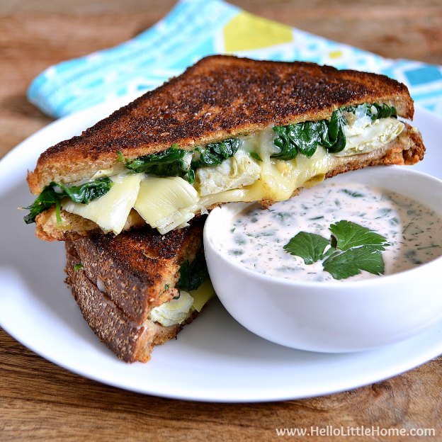 A Spinach and Artichoke Grilled Cheese served with Ranch dip on a white plate.