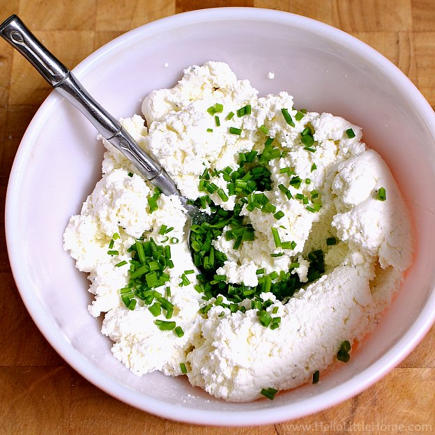 A spoon in a bowl of ricotta topped with chopped chives.
