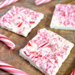 Candy canes and pieces of White Chocolate Peppermint Bark on a wood table.