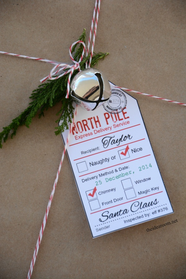 Closeup of a present topped with a bell, sprig of pine, and a printable label.