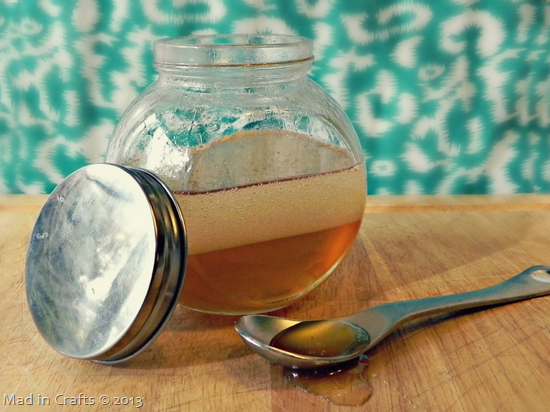 A container filled with a Coconut Honey Hair Mask next to a spoon on a wood board.