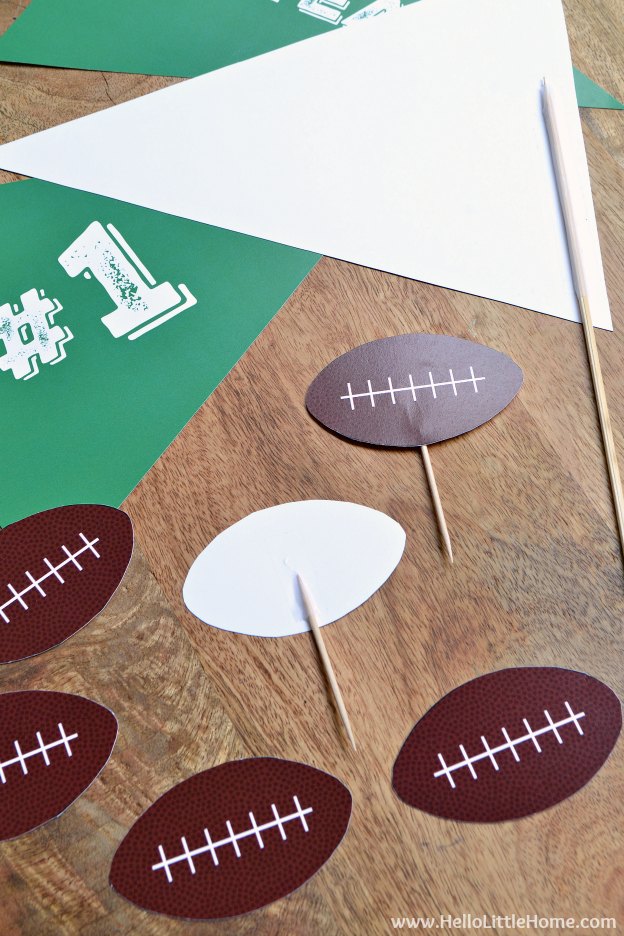 Mini football toppers attached to toothpicks on a wood table.