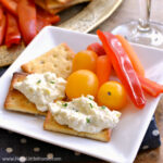 A plate with crackers, veggies, and creamy lemon artichoke spread.