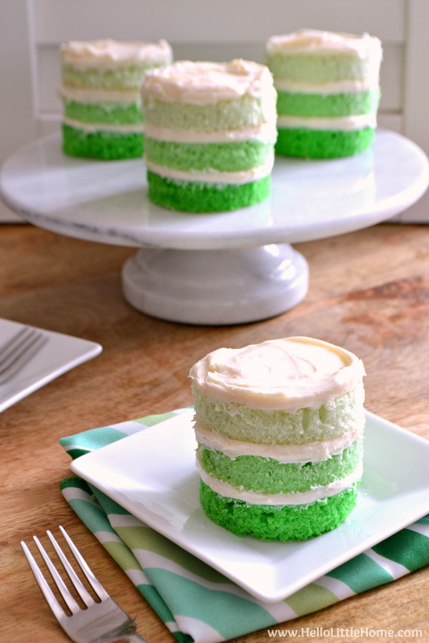 A mini green layer cake on a plate with more cakes in the background.