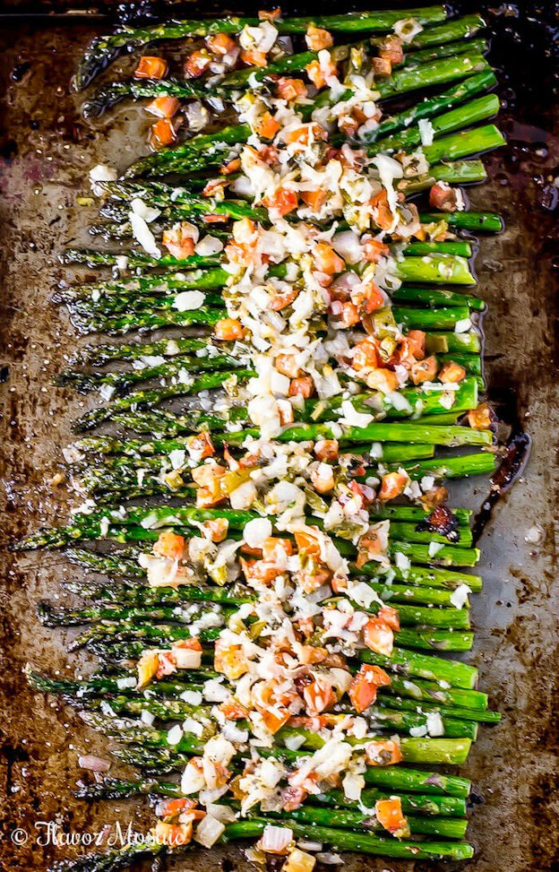 Roasted asparagus with a topping on a baking sheet.