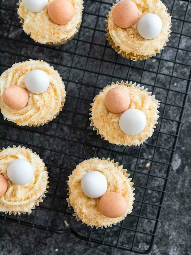 Cupcakes topped with frosting and candy eggs on a baking rack.