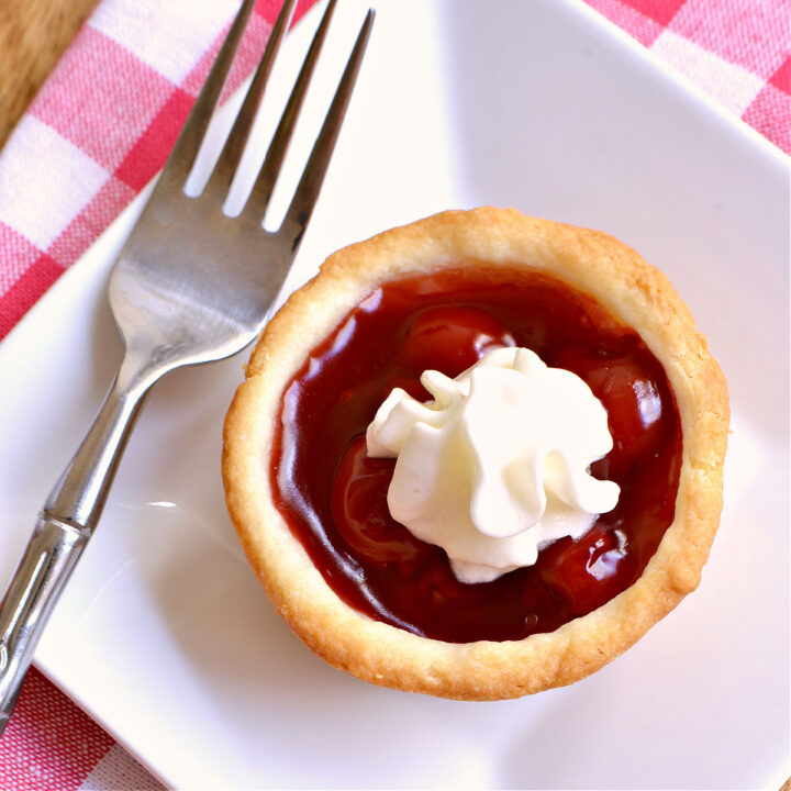 A mini cherry tart and a fork on a white plate.