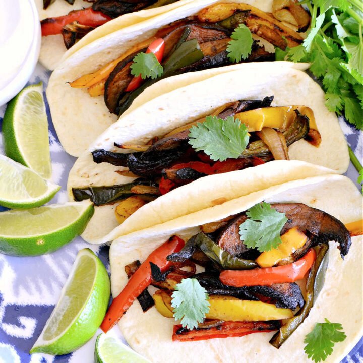 Veggie Fajitas served next to lime wedges on a blue tray.