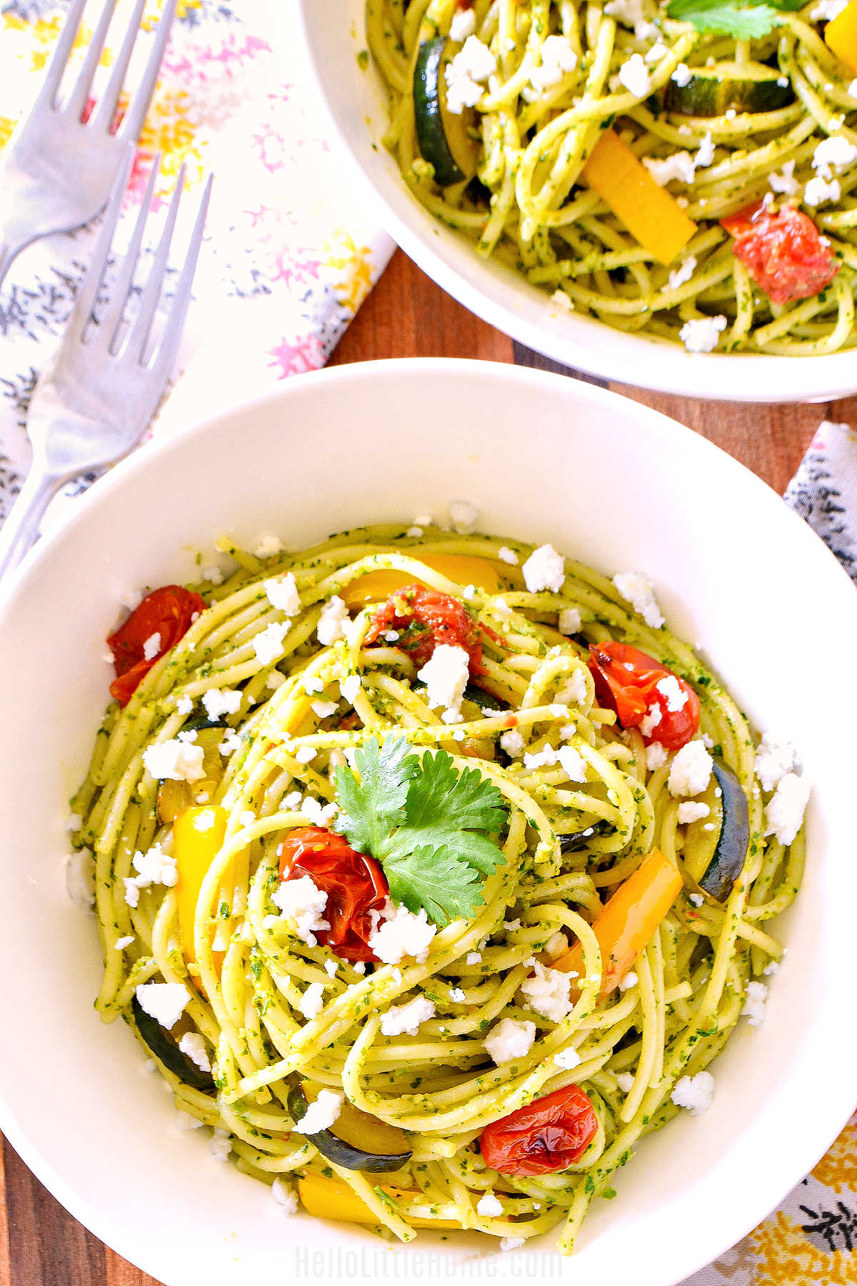 Two bowls of Coriander Pesto Pasta, napkins, and forks on a wood table.
