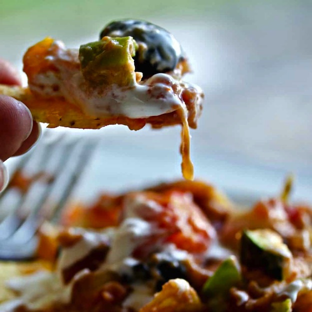 A hand lifting a nacho from a plate.