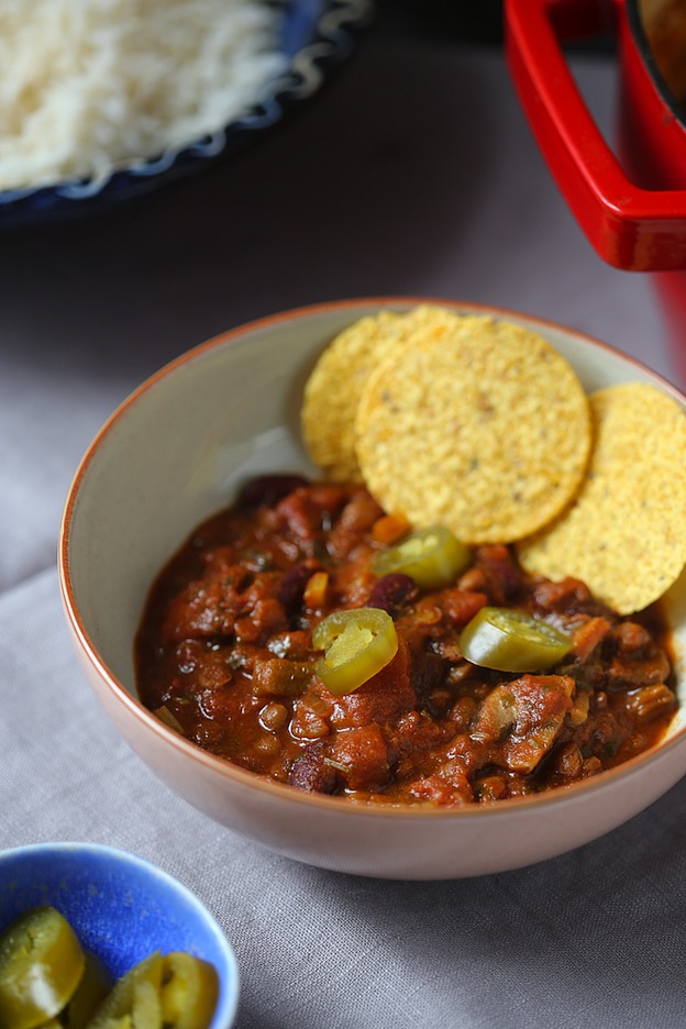 A bowl of lentil chili garnished with round tortilla chips.