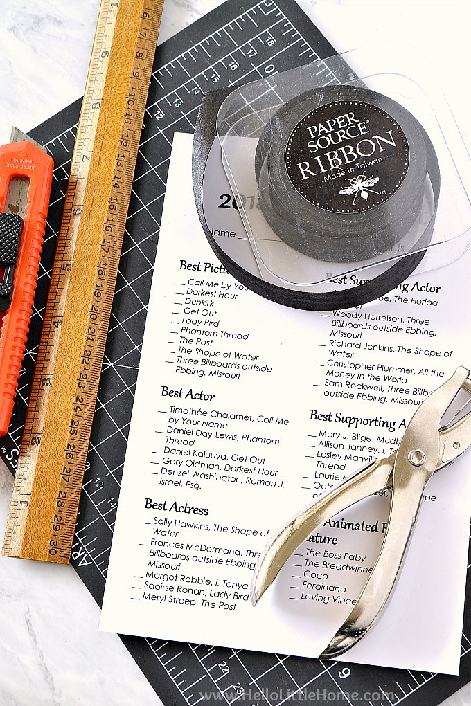 Supplies for assembling Oscar Ballot Printables: utility knife, ruler, cutting mat, ribbon, and a hole punch.