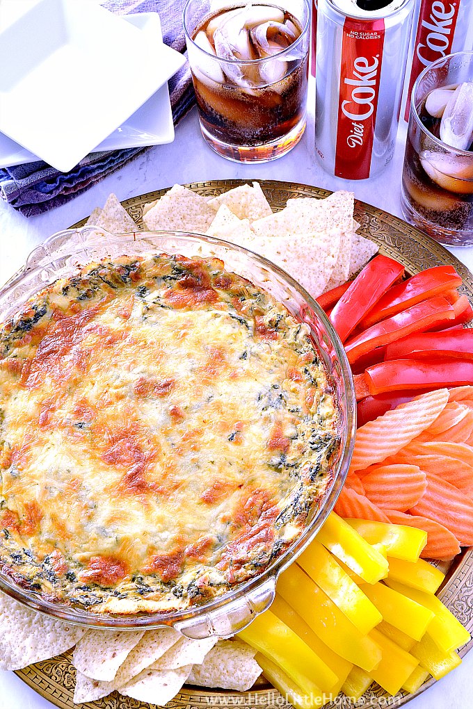 A table topped with a pan of Hot Spinach Dip, veggies, tortilla chips, plates, and Diet Coke.