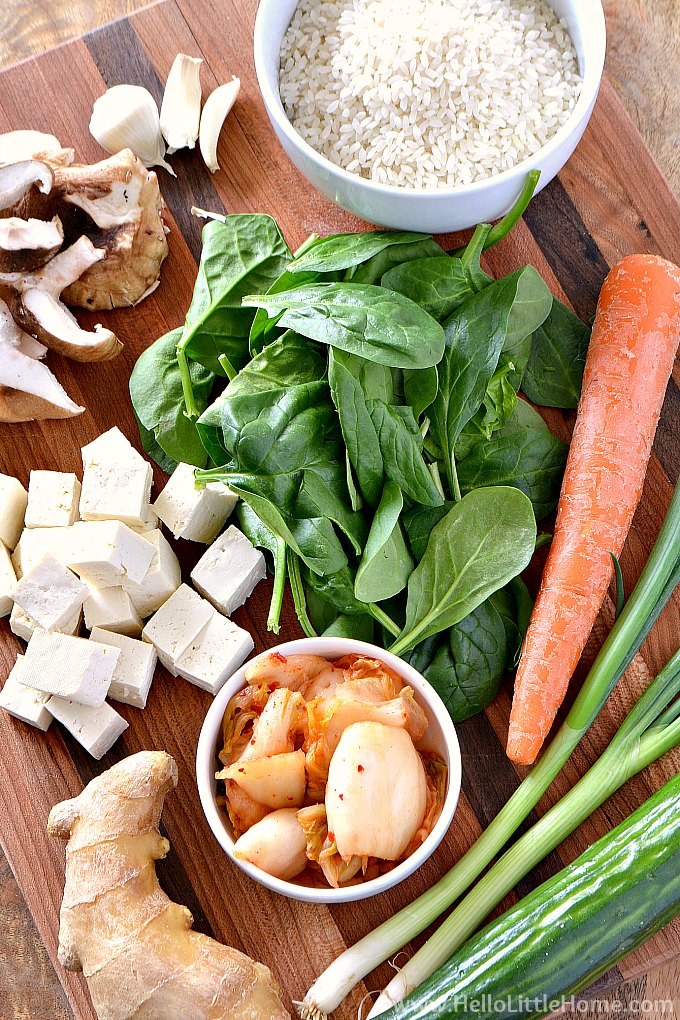 Ingredients for vegetarian bibimbap on a cutting board: rice, veggies, tofu, kimchi, ginger.