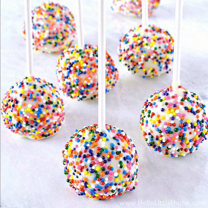Birthday Cake Pops covered sprinkles on a marble table.