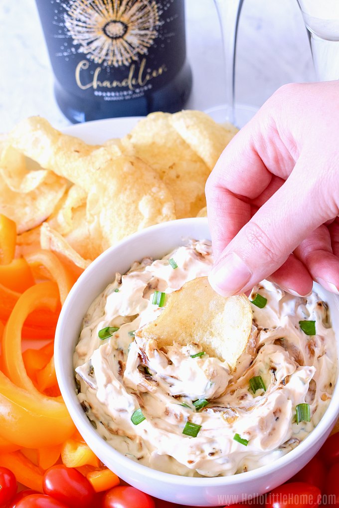 A hand dipping a chip into the homemade French Onion Dip.