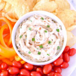 A bowl of Caramelized Onion Dip surrounded by chips and veggies.