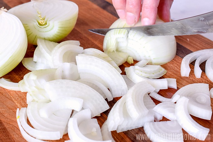A hand slicing the onions on a wood cutting board.