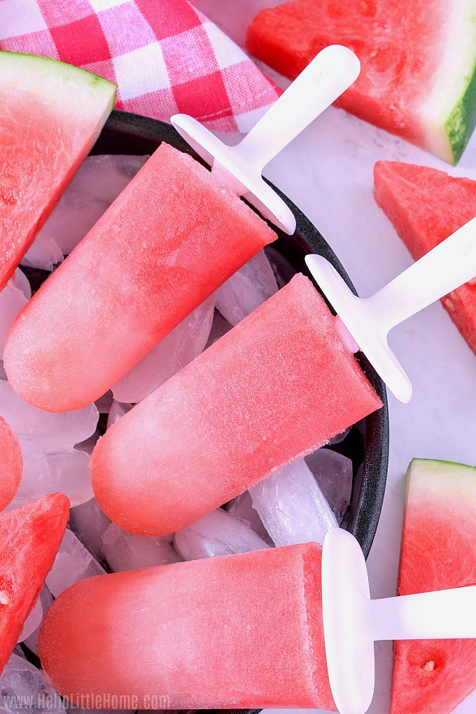 Half a tray of popsicles and watermelon slices on a white counter.