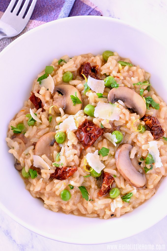 A bowl of Instant Pot Risotto with mushrooms, lemon, peas, tomatoes, and parmesan cheese.