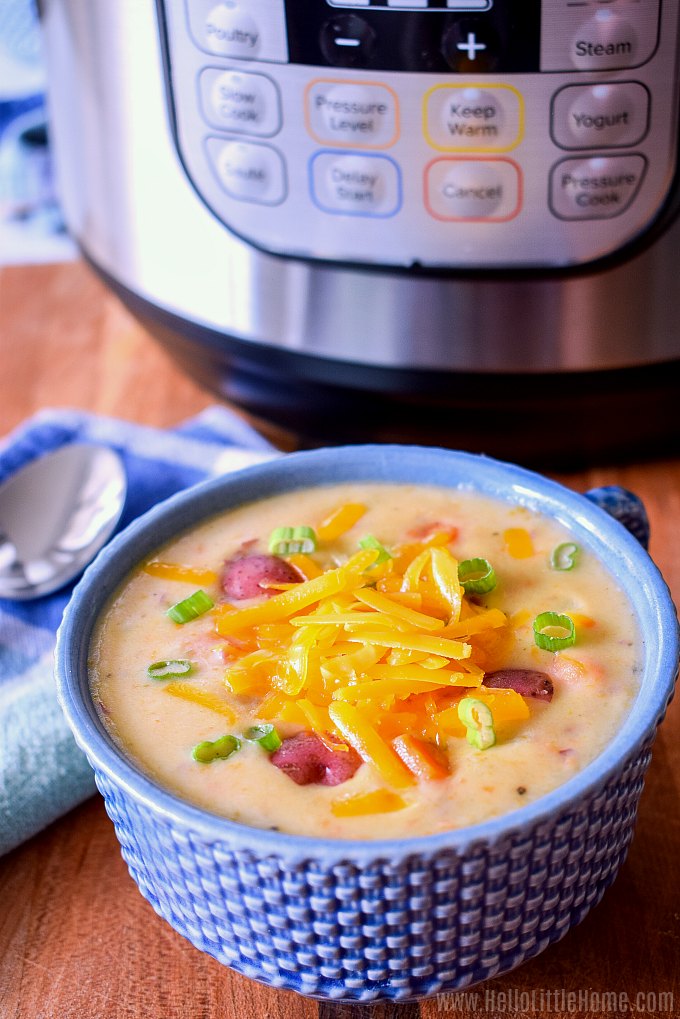 A bowl of potato soup on a wood table with an Instant Pot in the background.