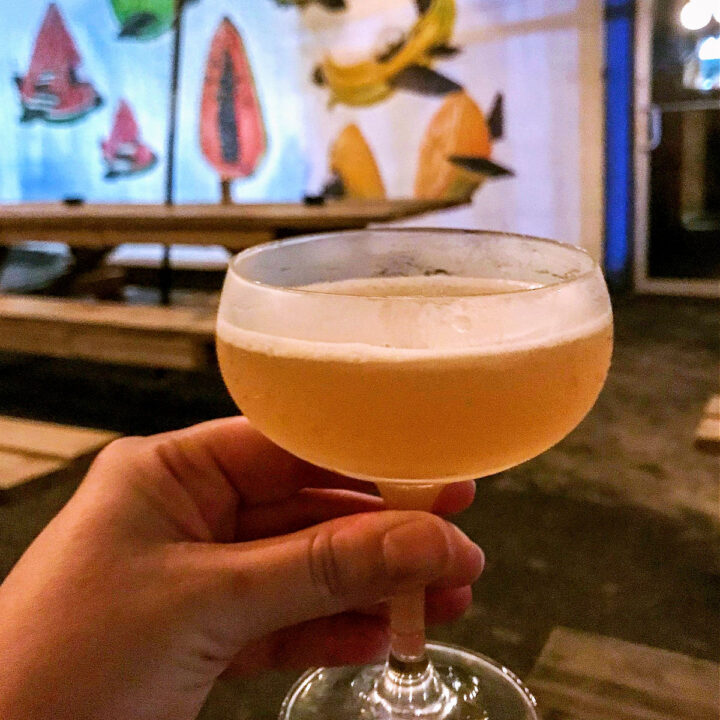 A hand holding a cocktail with a colorful mural in the background.