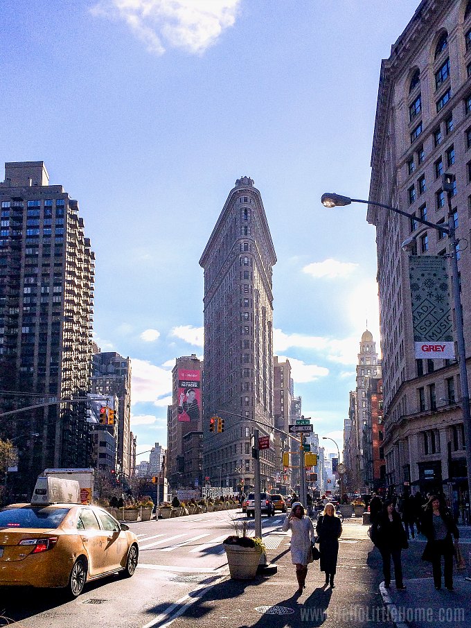 People walking on a sidewalk with the Flatiron Building in the background.