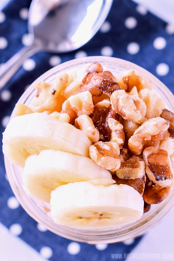 An overhead image of a jar of oatmeal topped with banana slices and walnuts.