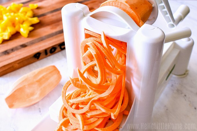 Spiralizing a sweet potato on a white marble counter.