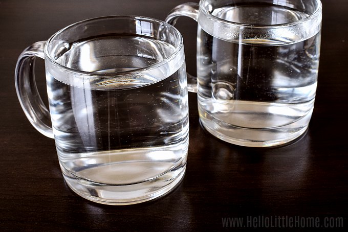 Two glass mugs filled with hot water on a table.