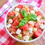 A bowl of Watermelon Quinoa Salad, napkin, and fork on a wood table.
