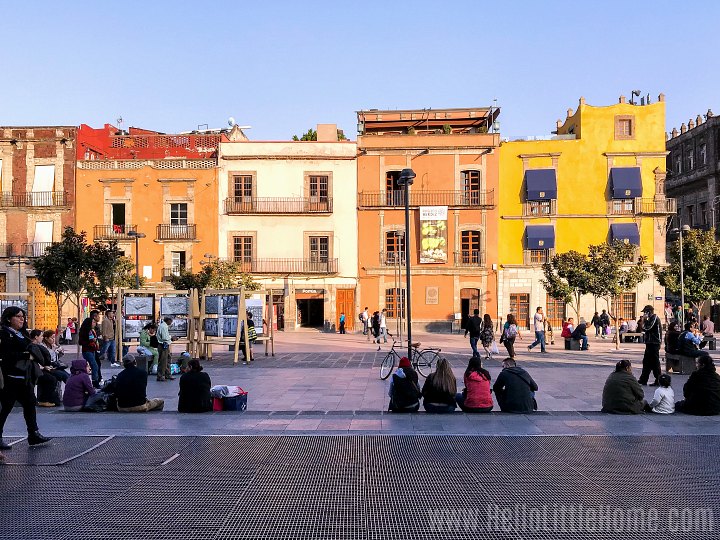 People sitting in front of a row of colorful historic buildings in the Centro Historico.