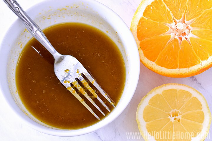 The dressing and a fork in a small bowl next to two orange halves.