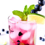 Closeup of the finished Blueberry Mojito garnished with mint, blueberries, and a lime wedge.