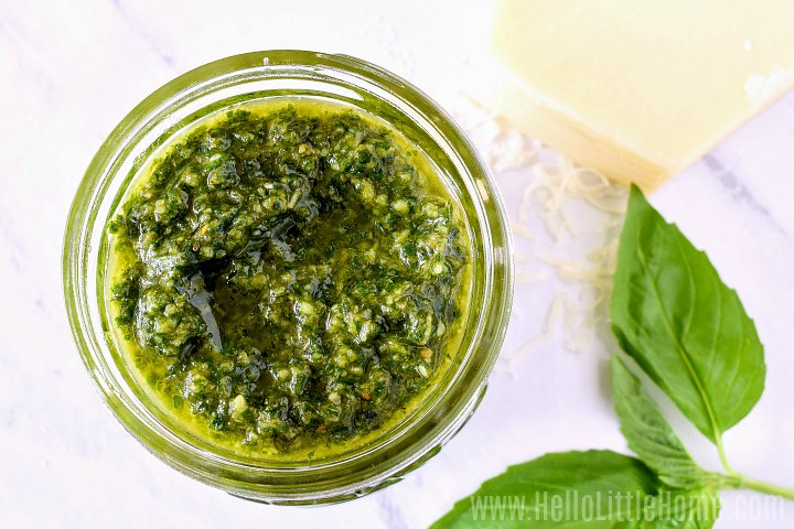 A jar of Pesto Sauce next to Parmesan cheese and basil leaves.