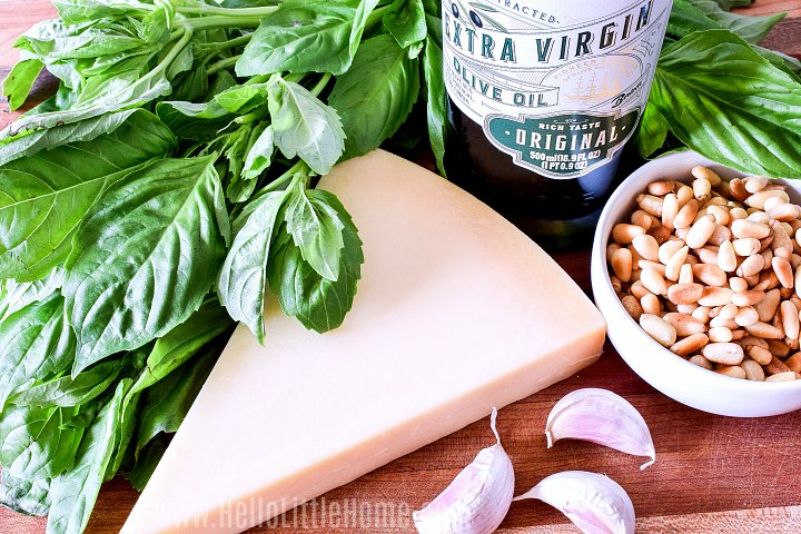 Pesto Pasta ingredients (fresh basil, nuts, garlic, Parmesan, olive oil) on a wood board.