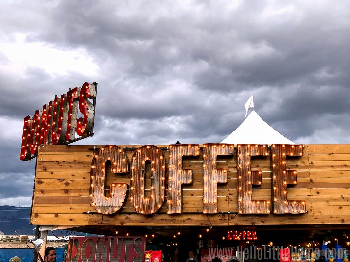A sign advertising coffee and donuts above a vendor booth.
