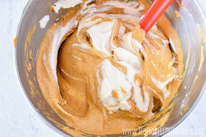 Mixing whipped cream into pumpkin cheesecake mixture with a spatula.