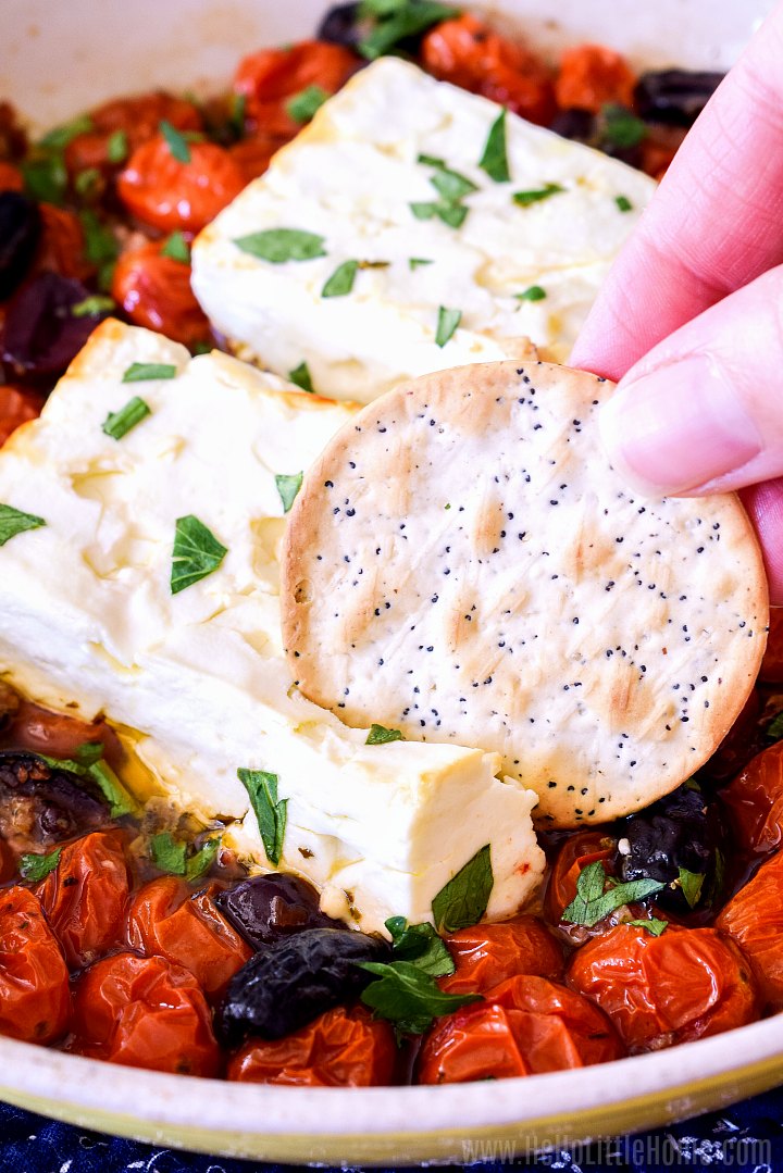 A hand sticking a cracker in Baked Feta Dip.