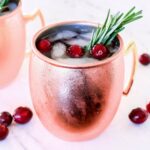 A Cranberry Moscow Mule served in a copper mug and garnished with rosemary.