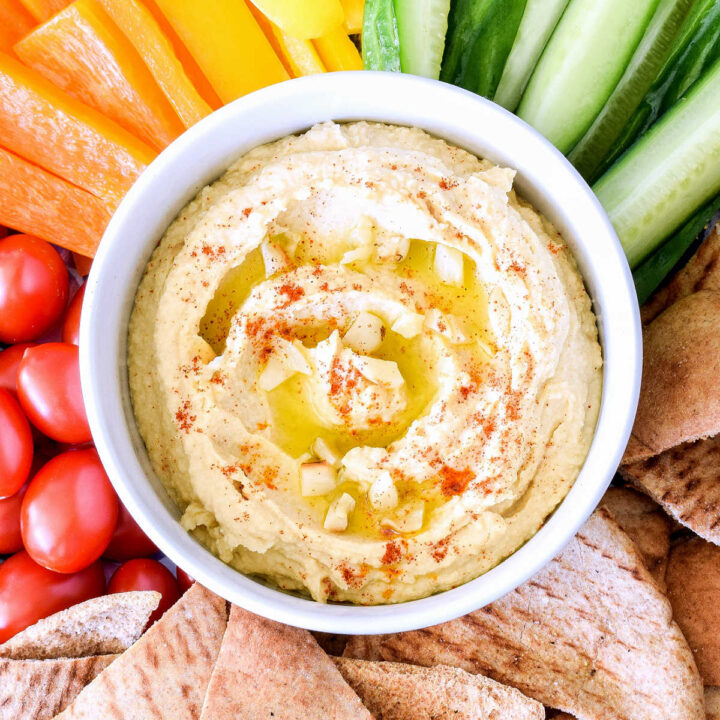 A bowl of Roasted Garlic Hummus surrounded by veggies and pita.