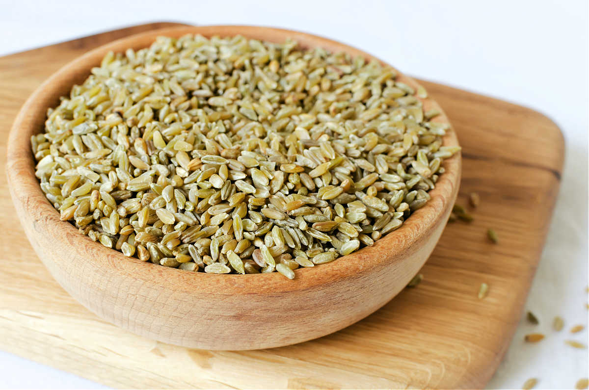 A bowl of uncooked freekeh on a wood cutting board.
